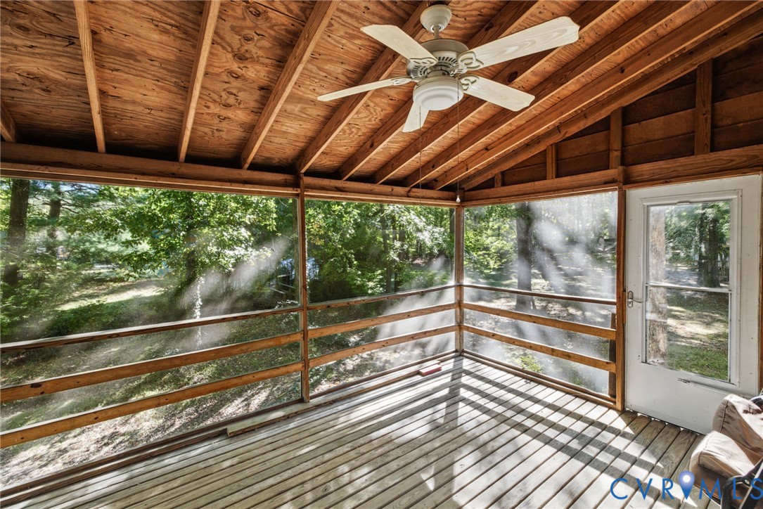 Screened porch featuring exposed wood beam rafters, wood-plank flooring, a ceiling fan with integrated lighting, and full-height mesh screening