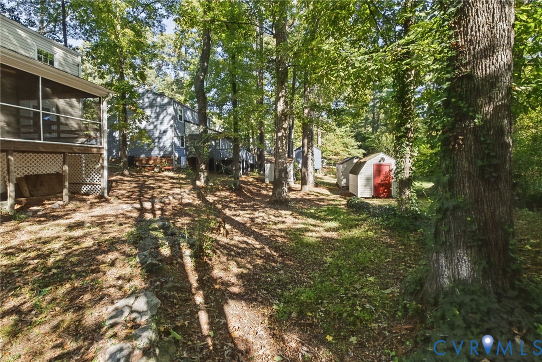 Wooded backyard featuring a screened-in porch, lattice skirting, and two detached storage sheds
