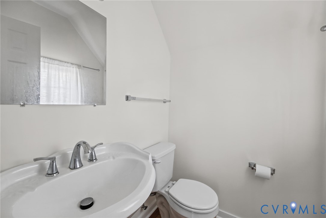 Wall-mounted frameless mirror, pedestal sink with chrome faucet, and standard toilet fixture