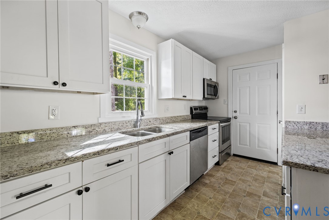 Kitchen featuring white shaker-style cabinetry, stone-finish countertops, stainless steel appliances, a double-basin undermount sink with a gooseneck faucet, and tiled flooring Kitchen featuring white shaker-style cabinetry, stone-finish countertops, stainless steel appliances, a double-basin undermount sink with a gooseneck faucet, and tiled flooring