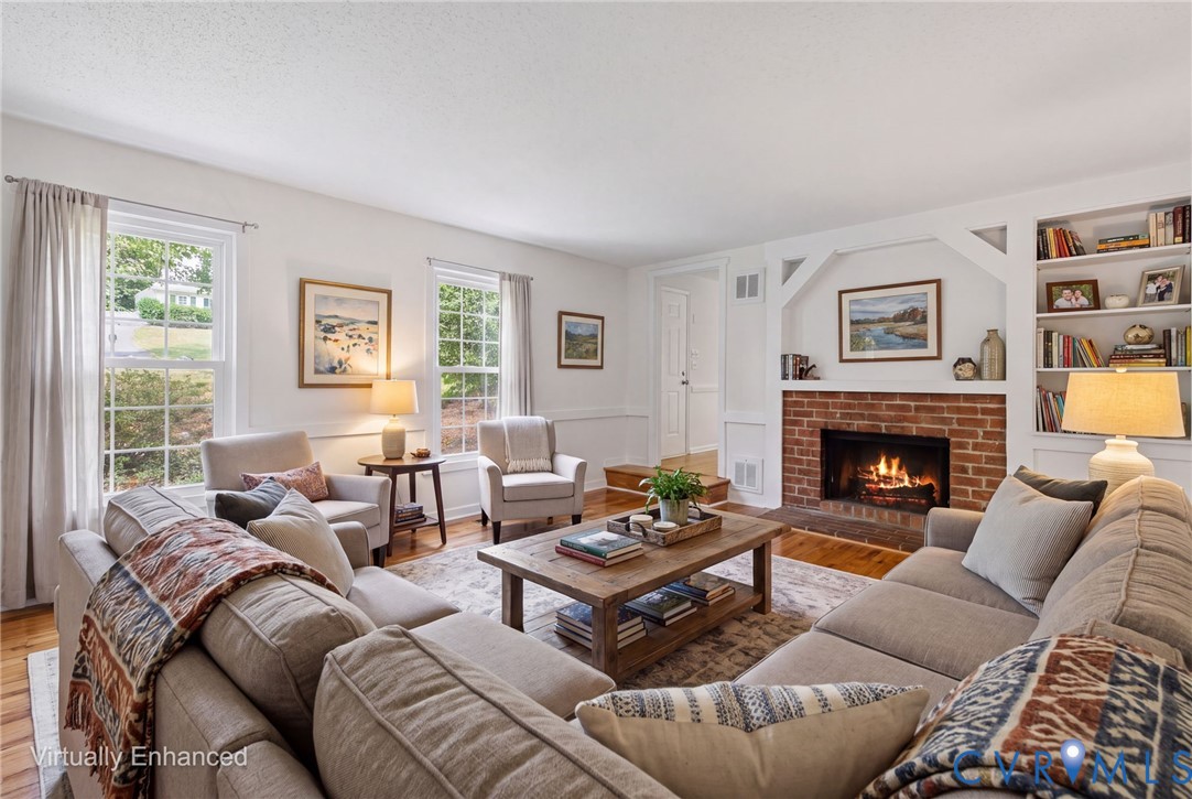 Living room featuring wood-finish flooring, a brick fireplace, built-in shelving, and large double-hung windows