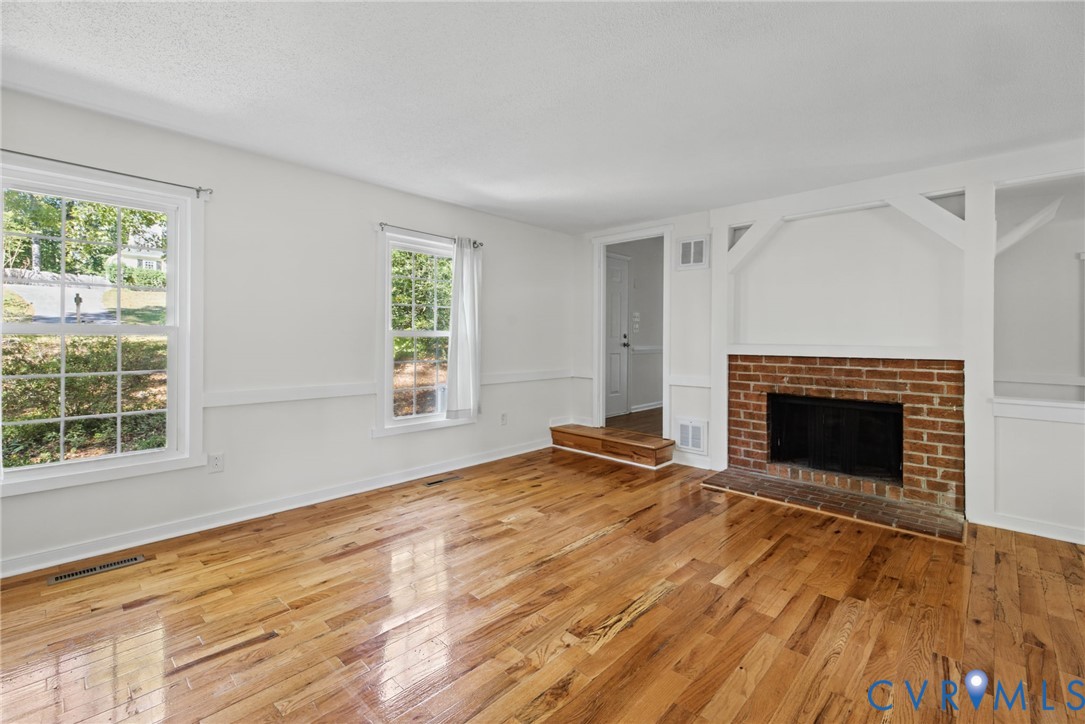 Living space featuring wood-finish flooring, a red brick fireplace, decorative woodwork detailing, and multiple windows