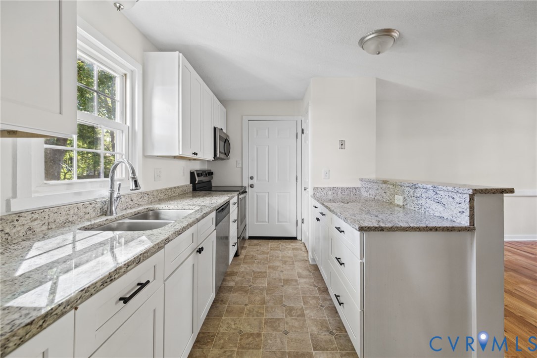 Kitchen featuring white cabinetry, light-toned stone countertops, stainless steel appliances, dual-basin stainless steel sink, and tile flooring Kitchen featuring white cabinetry, light-toned stone countertops, stainless steel appliances, dual-basin stainless steel sink, and tile flooring