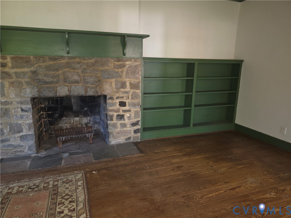 Stone fireplace with a substantial painted wood mantel, custom built-in shelving, slate hearth, and dark wood-finish flooring