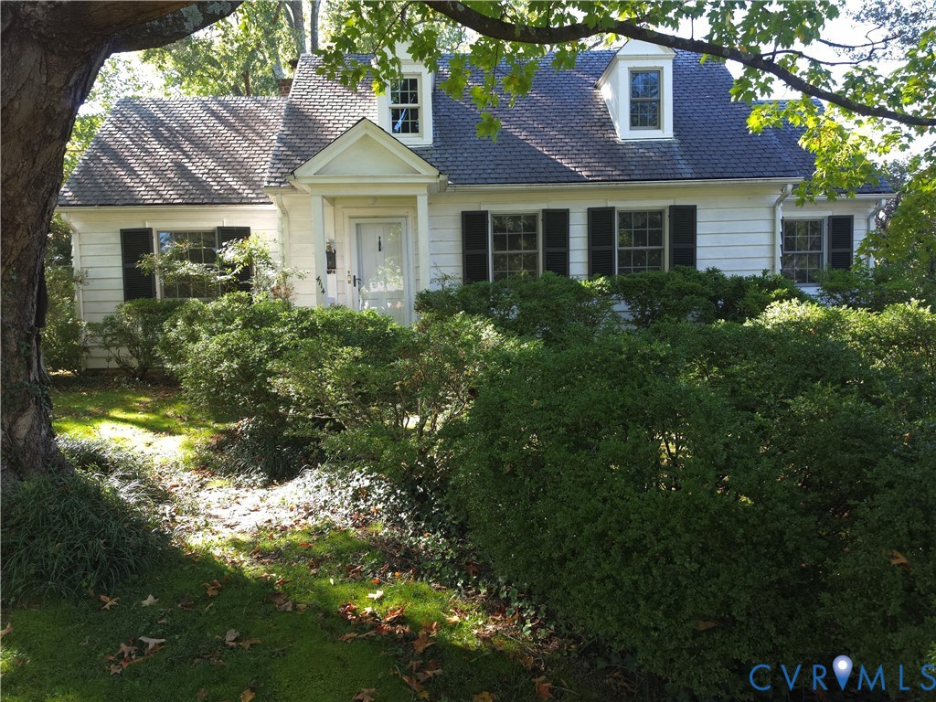Cape Cod architecture featuring white siding, dark shutters, two dormer windows, and a covered front entryway