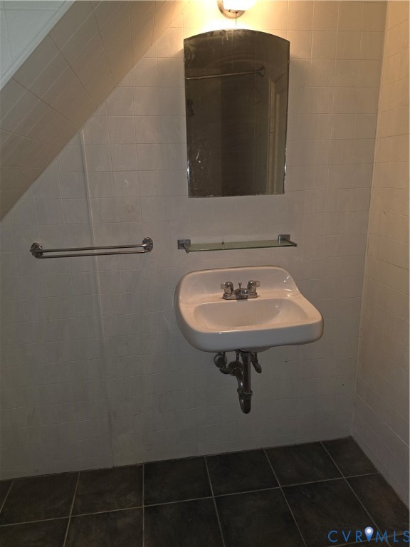 Wall-mounted porcelain sink with chrome fixtures, glass shelf, arched mirror, and tiled wall surfacing, complemented by dark ceramic floor tiling