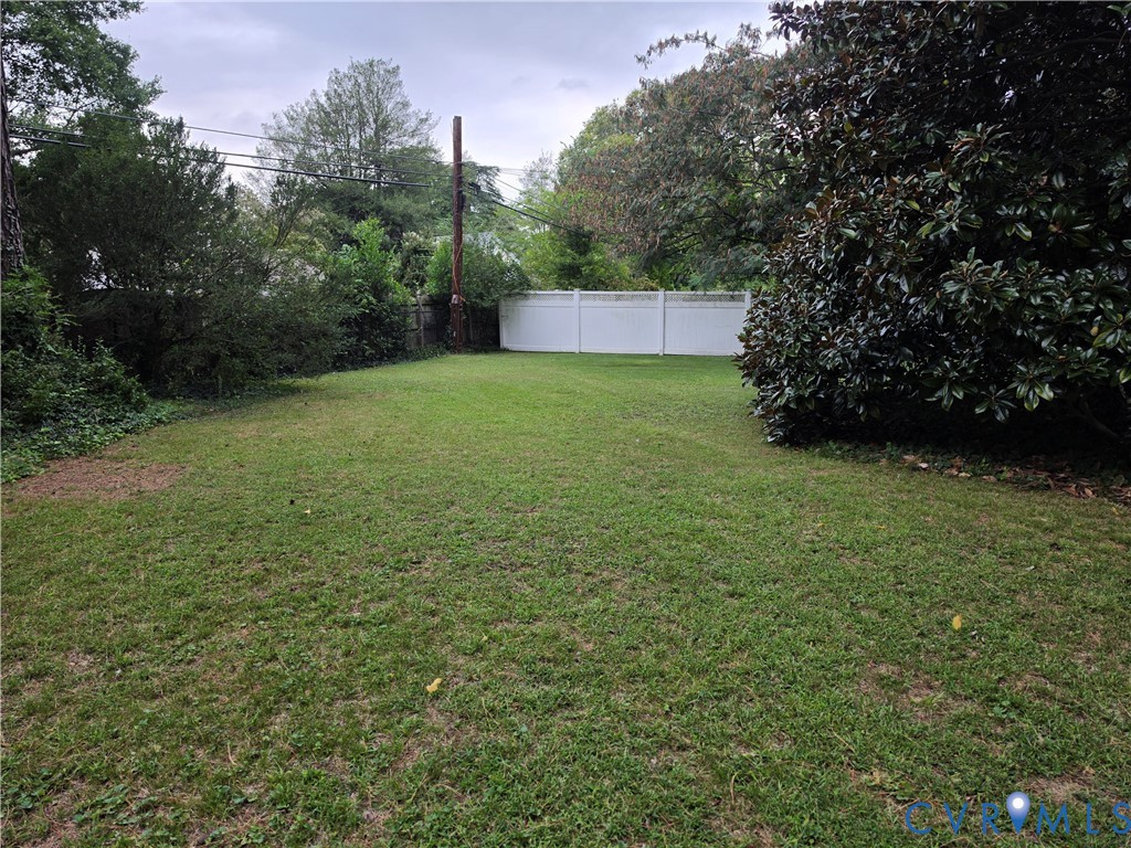 Expansive backyard featuring a level lawn, mature foliage, and a white privacy fence