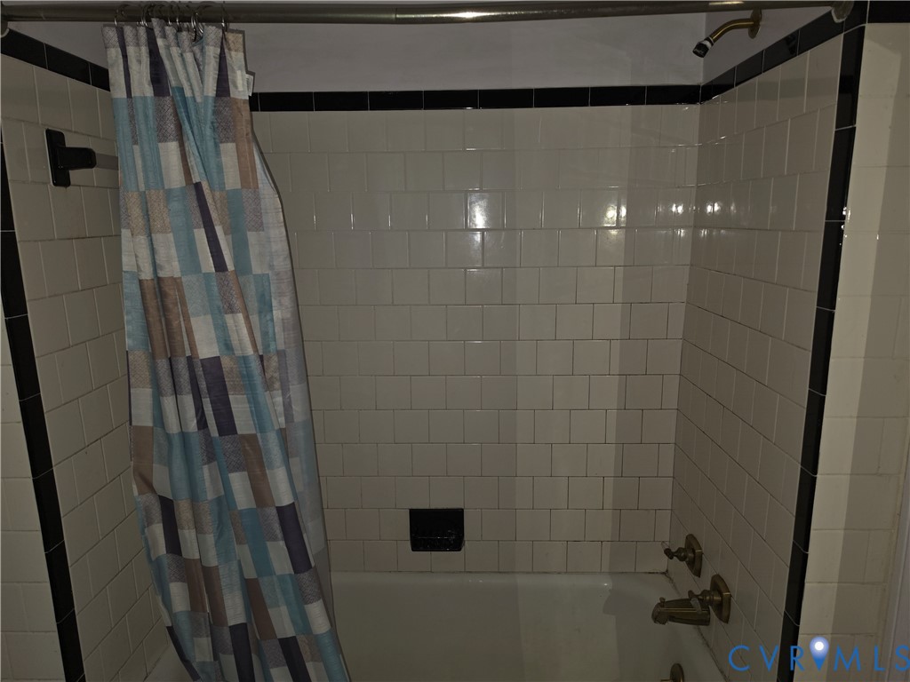 Shower and tub combination featuring cream-colored wall tiles, a contrasting black accent tile border, and metallic fixtures