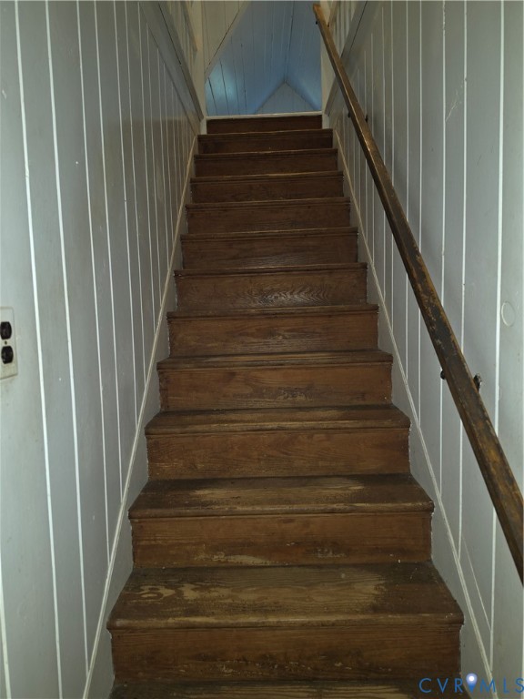 Staircase featuring wood treads, vertical paneled wall treatments, and a mounted wooden handrail