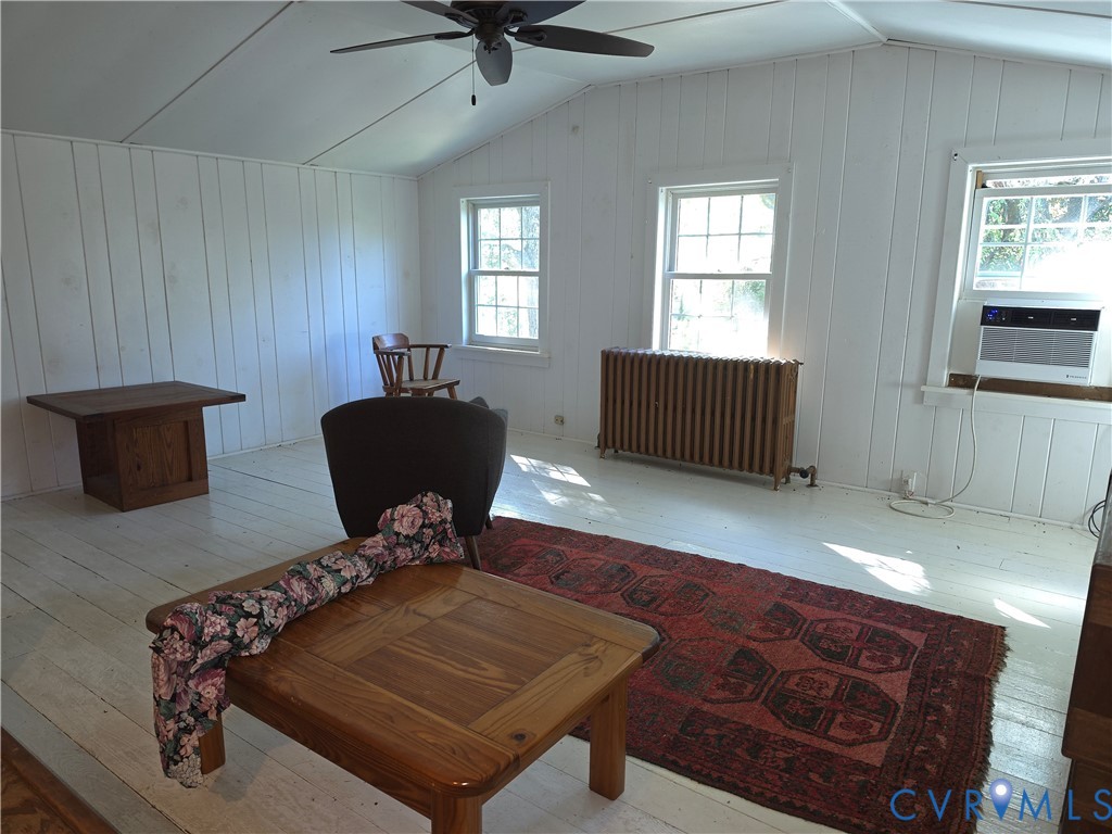 Vaulted ceilings with vertical paneling, painted wood-finish flooring, multi-pane windows, and a classic cast-iron radiator