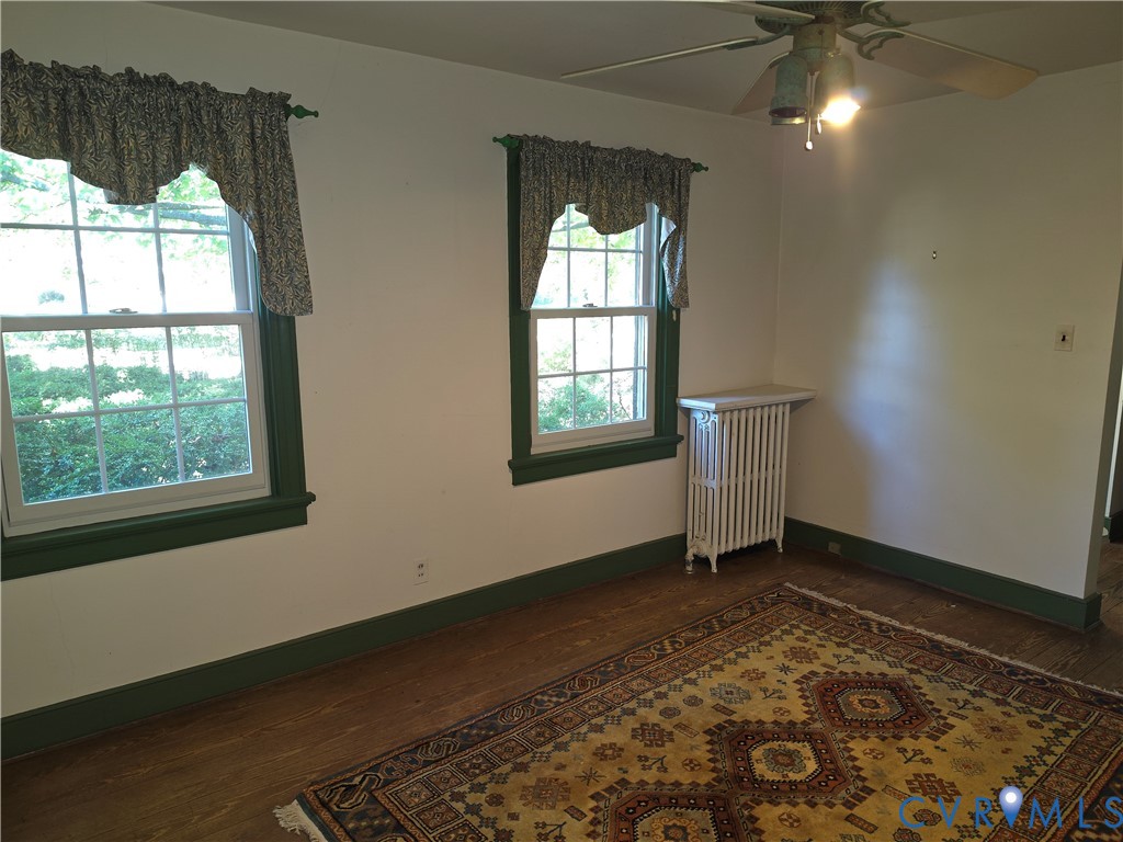 Interior space featuring hardwood flooring, multi-pane windows with colored casings, and a vertical cast-iron radiator