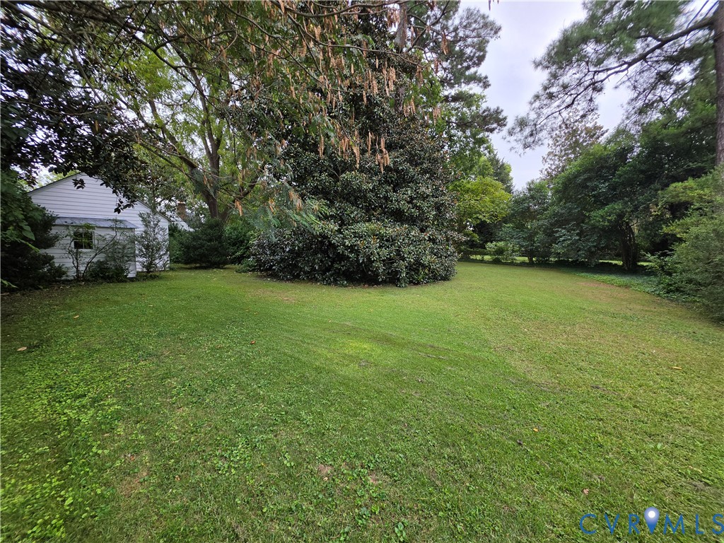Expansive backyard featuring mature trees, established landscaping, and white horizontal siding exterior