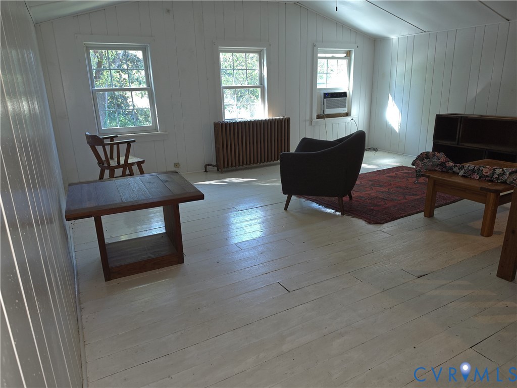 Interior room featuring white-painted vertical plank wall paneling, painted wood-finish flooring, three double-hung windows, and a classic metal radiator