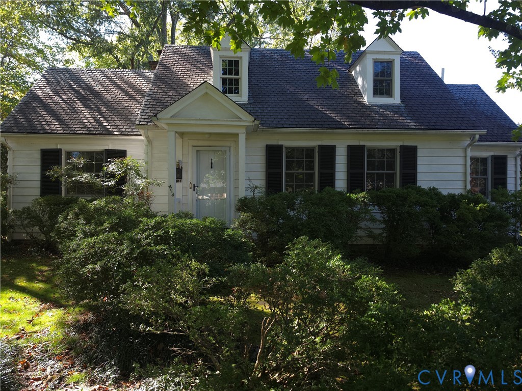 Raised Ranch/Cape Cod exterior featuring white horizontal siding, dark decorative shutters, a peaked entry portico, and two dormer windows