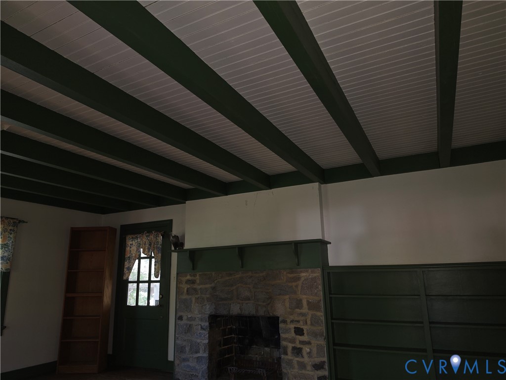 Exposed dark-finished ceiling beams with white beadboard paneling, floor-to-ceiling stone fireplace, and built-in wood shelving