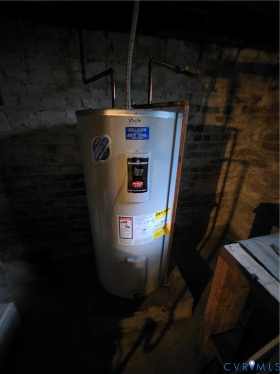 Electric water heater unit featuring copper plumbing lines and exposed masonry wall finish