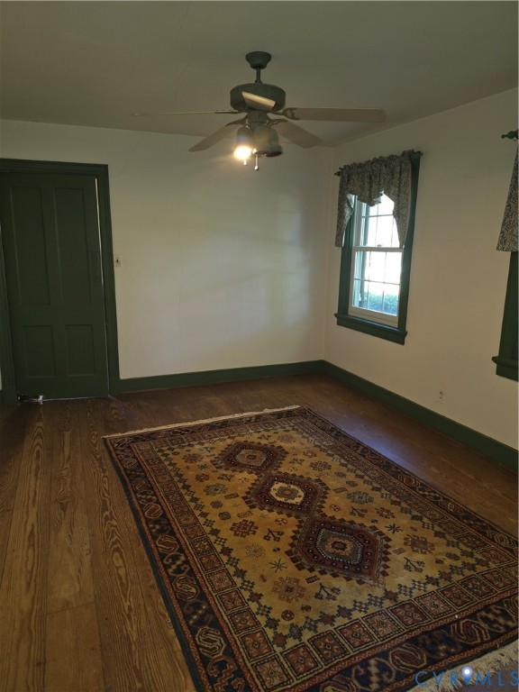 Room featuring wood-finish flooring, a multi-panel door with dark trim, dual windows with decorative casing, and a ceiling-mounted light fixture with fan