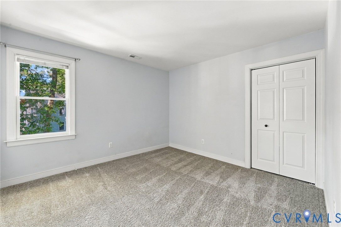 Bedroom 3 with neutral new carpeting, closet, and views of the surrounding greenery.