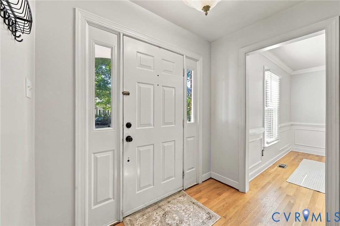 Bright and welcoming entryway featuring hardwood floors and a front door flanked by sidelights.
