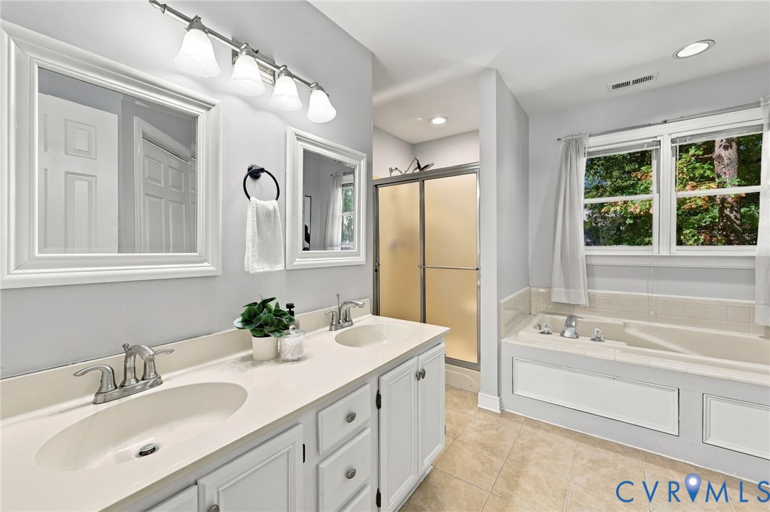 En-suite bathroom featuring a double-sink vanity, soaking tub, separate shower, and natural light.