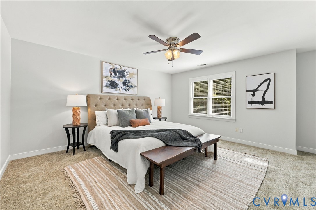 Spacious primary suite featuring neutral finishes, ceiling fan, and abundant natural light from double windows.