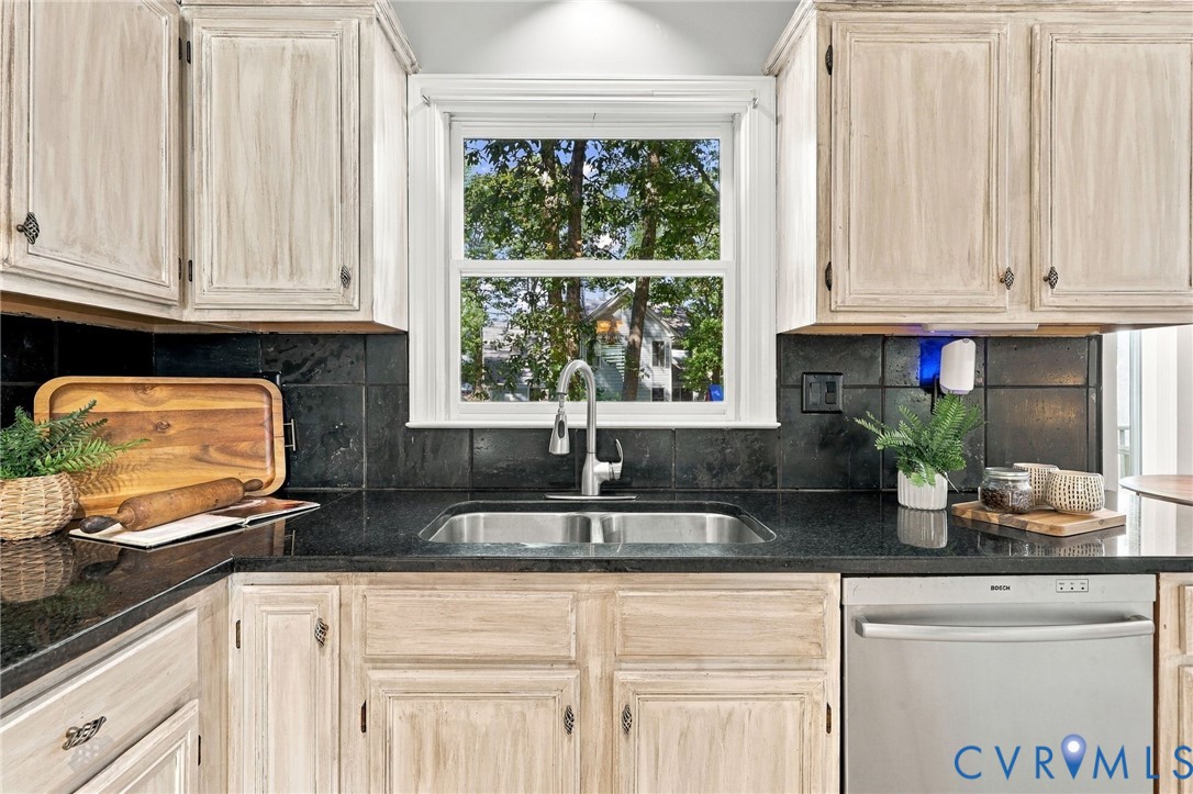 Kitchen featuring granite countertops, tile backsplash and a window overlooking the backyard.