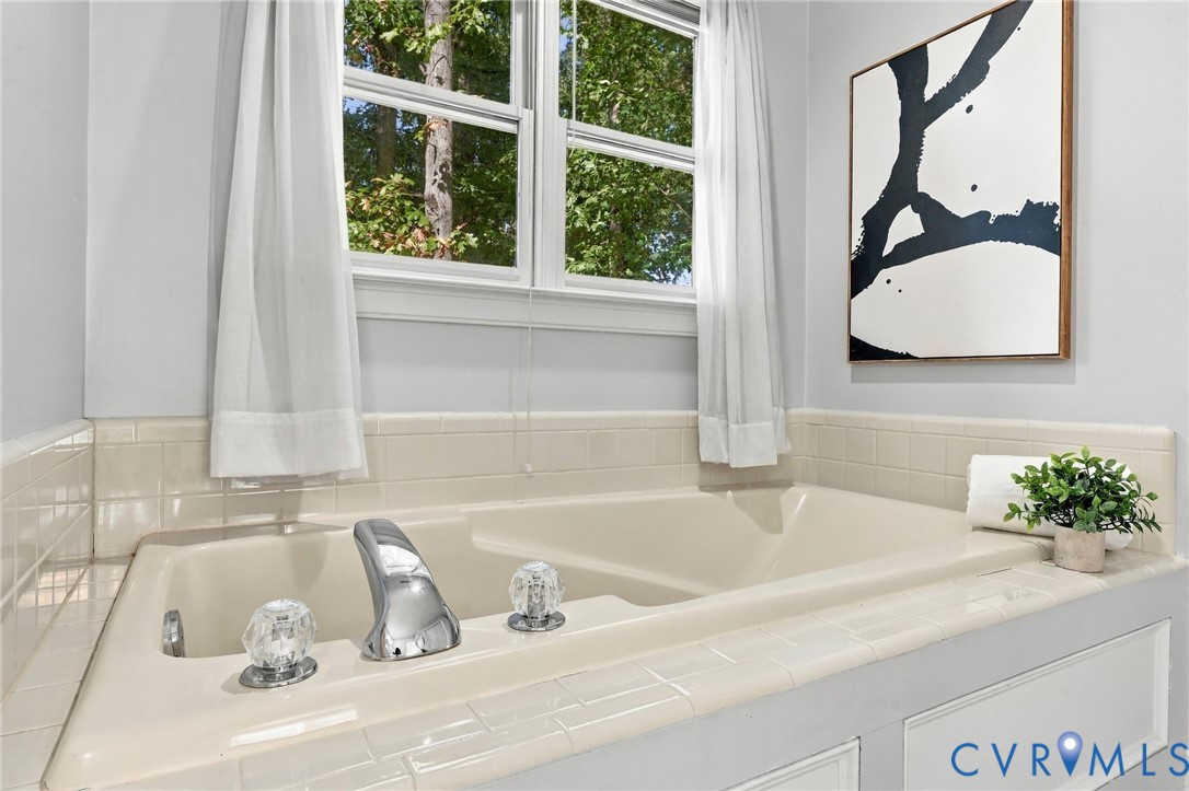 Relaxing soaking tub with tile surround and a large window overlooking the surrounding greenery.
