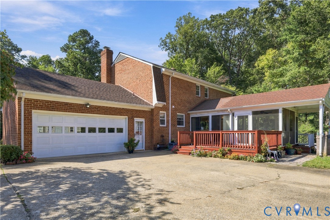 Brick exterior featuring an attached two-car garage, expansive concrete driveway, elevated wood deck, and a screened-in porch with a covered patio area
