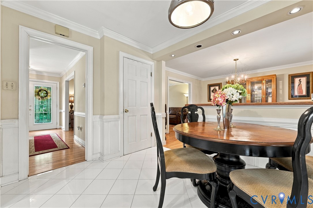 Dining area featuring white ceramic tile flooring, crown molding, white wainscoting, and recessed ceiling lighting