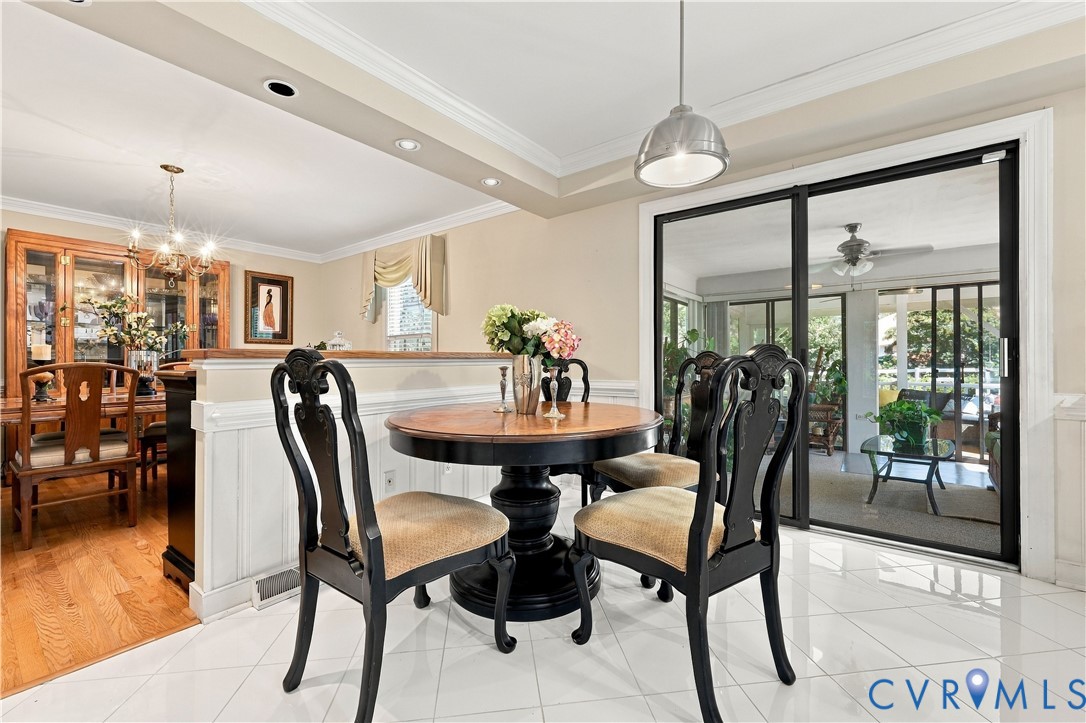Dining area featuring tile flooring, white wainscoting, crown molding, a modern pendant light, and black-framed sliding glass doors