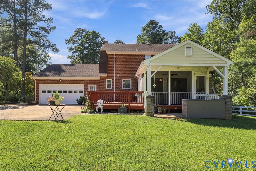 Brick exterior residence featuring a covered screened porch, an expansive raised wood deck, a two-car attached garage, and a manicured lawn