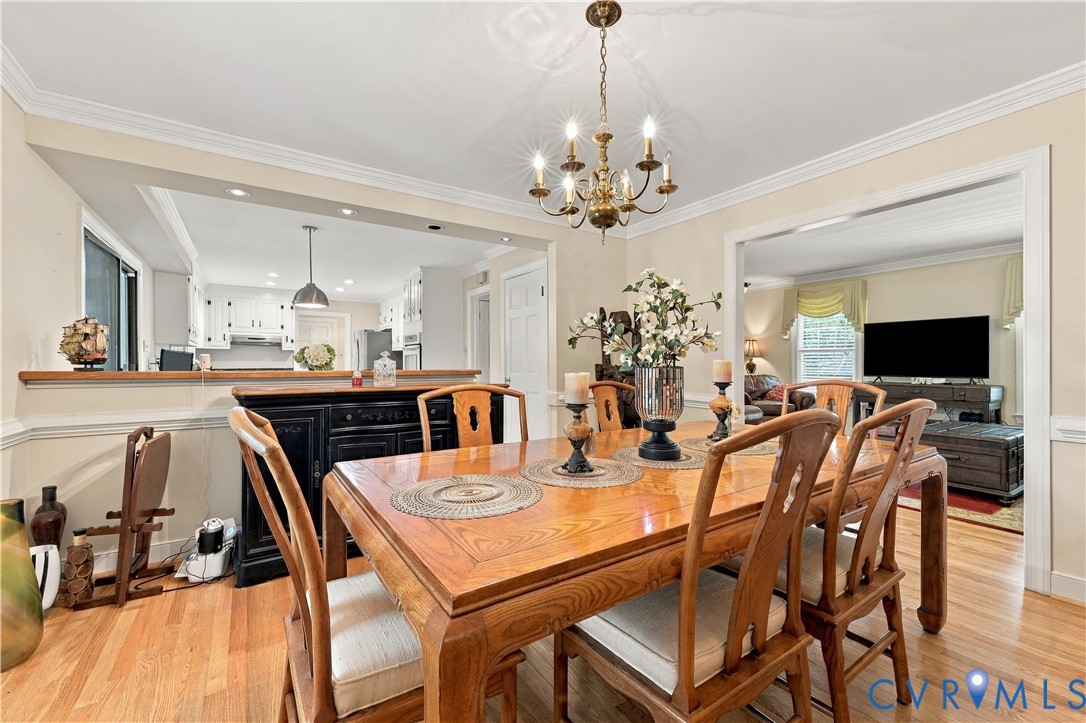 Dining area featuring hardwood flooring, crown molding, chair rail detailing, and a multi-arm chandelier