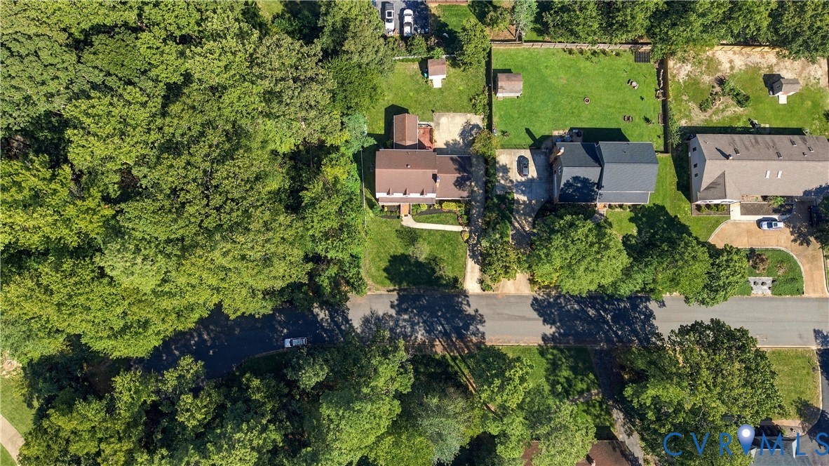 Aerial perspective of a multi-level residence featuring a paved driveway, a rear deck, and a detached structure, all situated on a lot with mature trees and expansive grass lawn