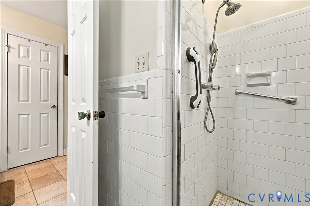 Walk-in shower enclosure with white subway tile surround, integrated shower head, grab bars, and recessed soap niche