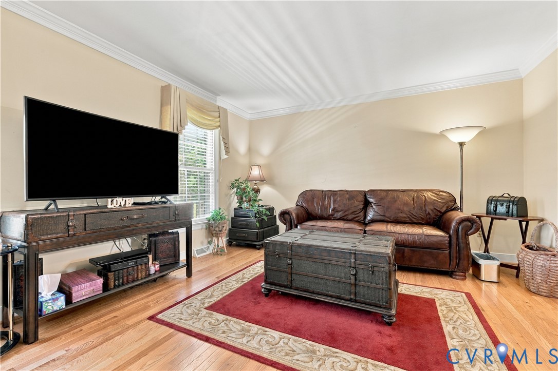 Living area featuring wood-finish flooring, crown molding, and a single-pane window with a valance
