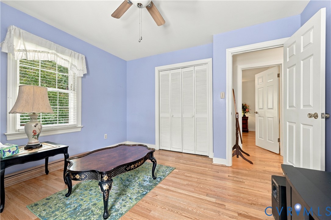 Room featuring wood-finish flooring, a multi-pane window with a valance, louvered bi-fold closet doors, and a ceiling-mounted fan