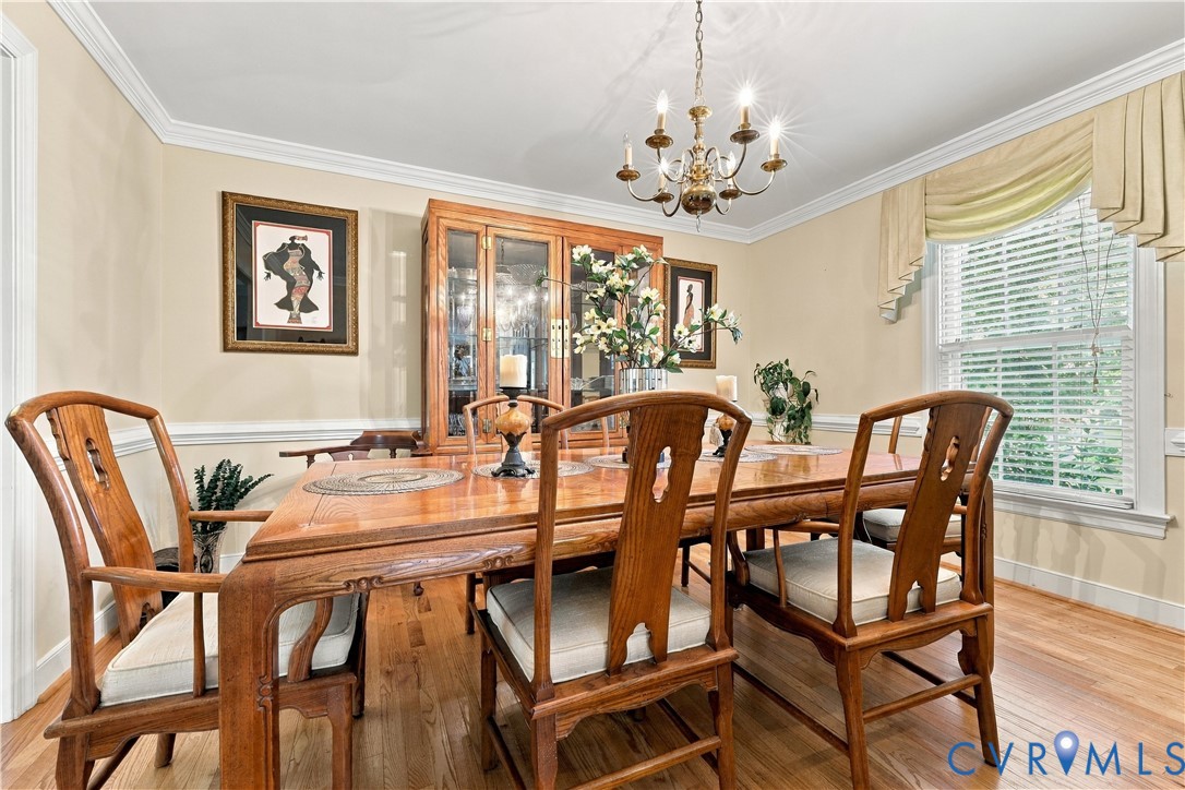 Dining space featuring wood-finish flooring, crown molding, chair rail trim, and a classic multi-light chandelier