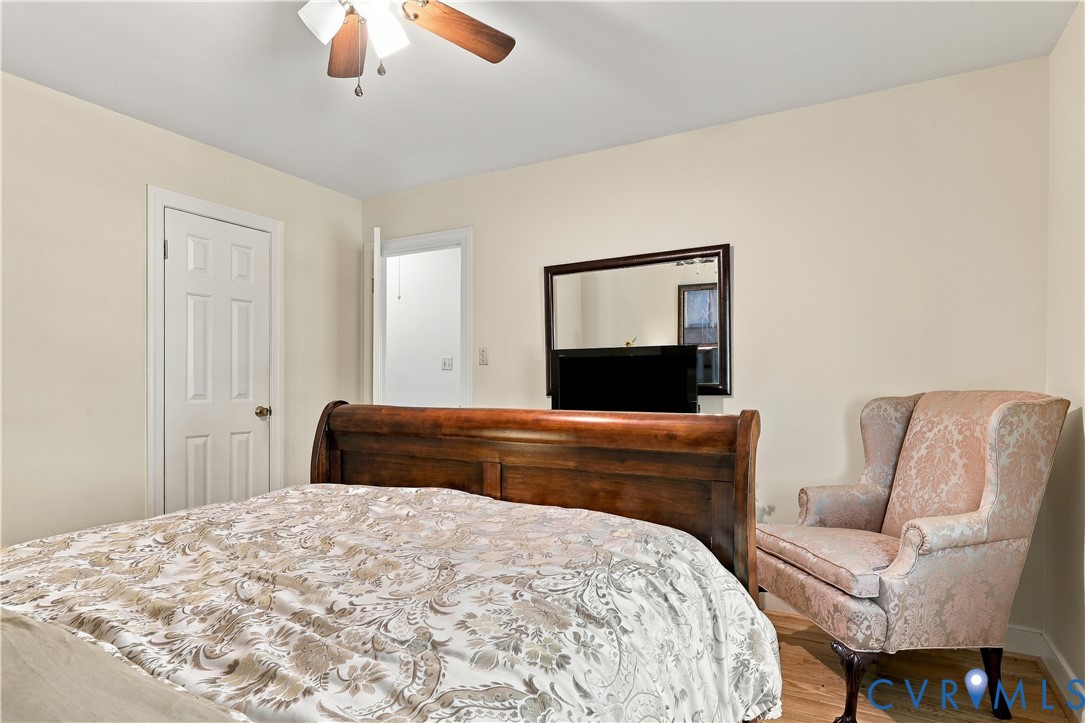 Neutral-toned interior walls featuring a six-panel door, light wood-finish flooring, and a ceiling-mounted light fixture with a three-blade fan