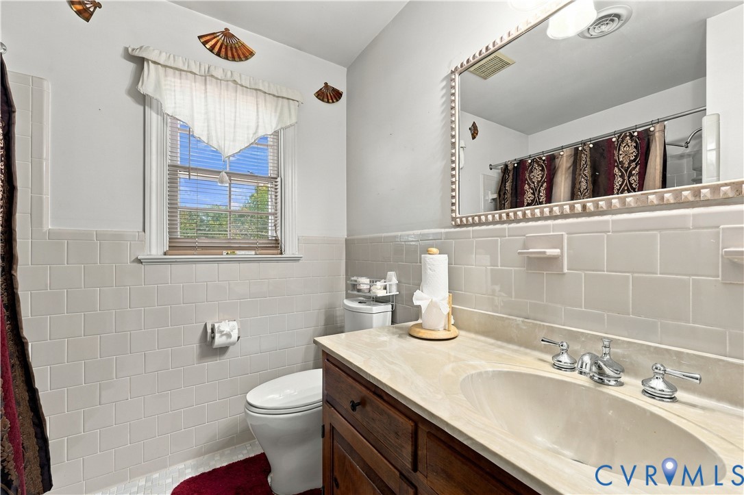 Bathroom featuring a wood-finish vanity with a light-toned countertop, integrated oval basin, large framed mirror, and cream-colored wall tile