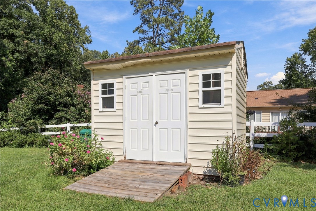 Exterior storage structure featuring light-colored horizontal siding, a gabled roof, dual entry doors, and a wood-slatted access ramp