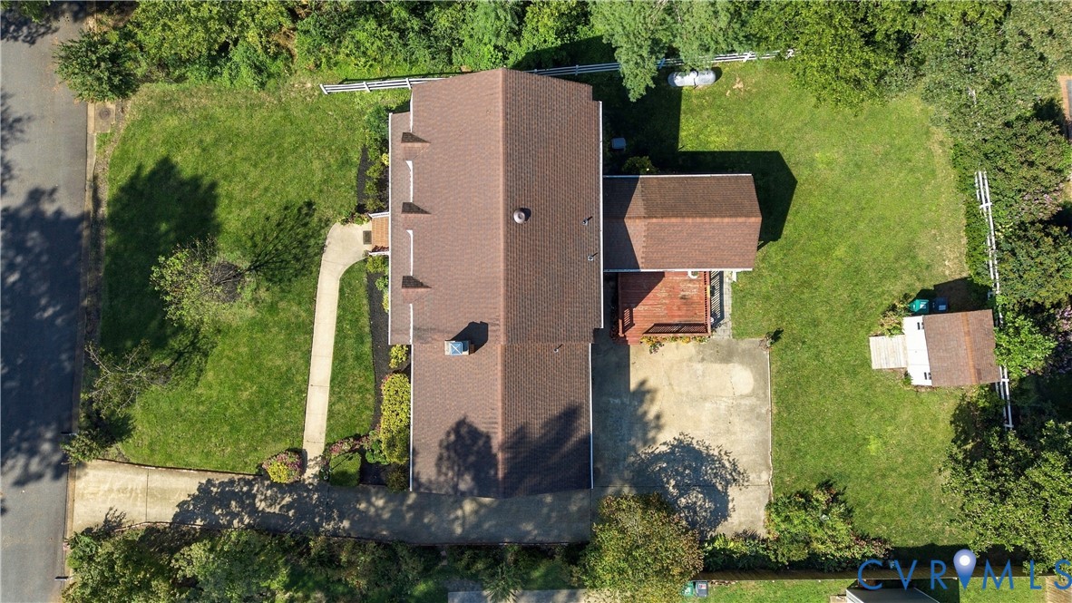 Aerial view featuring a multi-level structure with a gabled roof, an elevated wooden deck, a concrete driveway, and a detached storage shed situated on a spacious lot