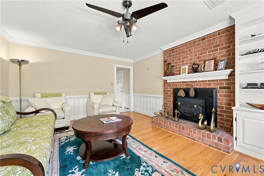 Red brick fireplace with a wood-burning insert and mantel, built-in floor-to-ceiling shelving, wood-finish flooring, and crown molding