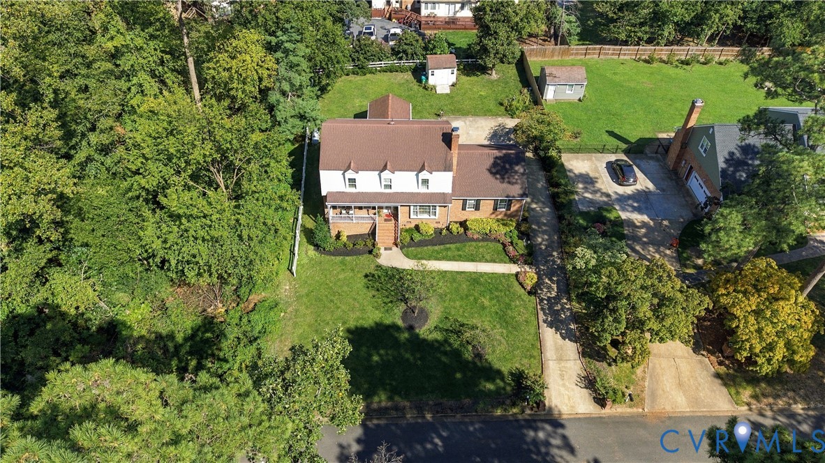 Two-story colonial exterior featuring a brick and siding facade, a covered front porch, a multi-gabled roofline, and an expansive lawn with mature trees
