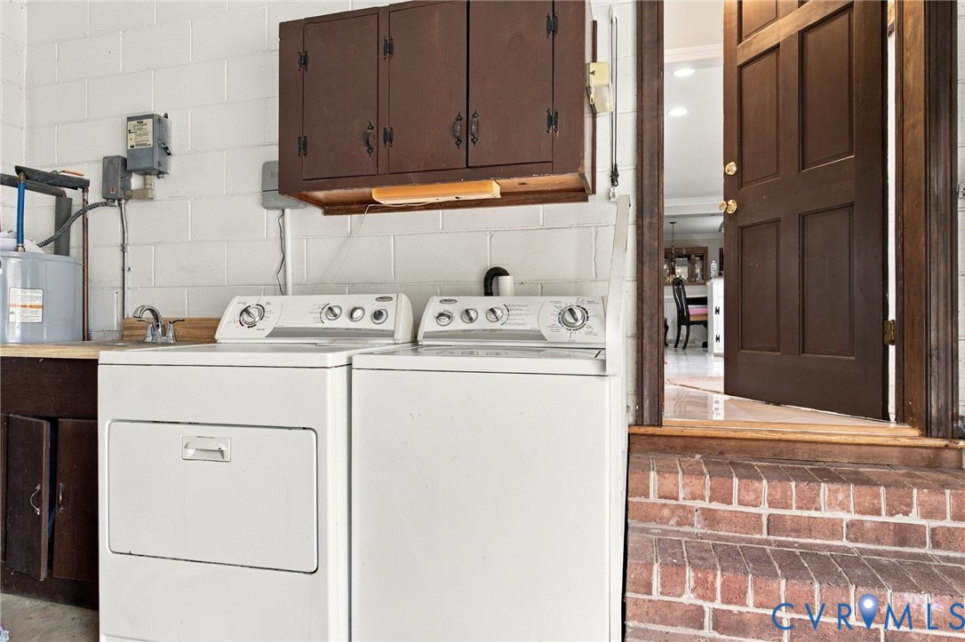Utility area featuring painted masonry walls, built-in wooden cabinetry, a stainless steel sink, and brick-faced steps leading to a raised entry door