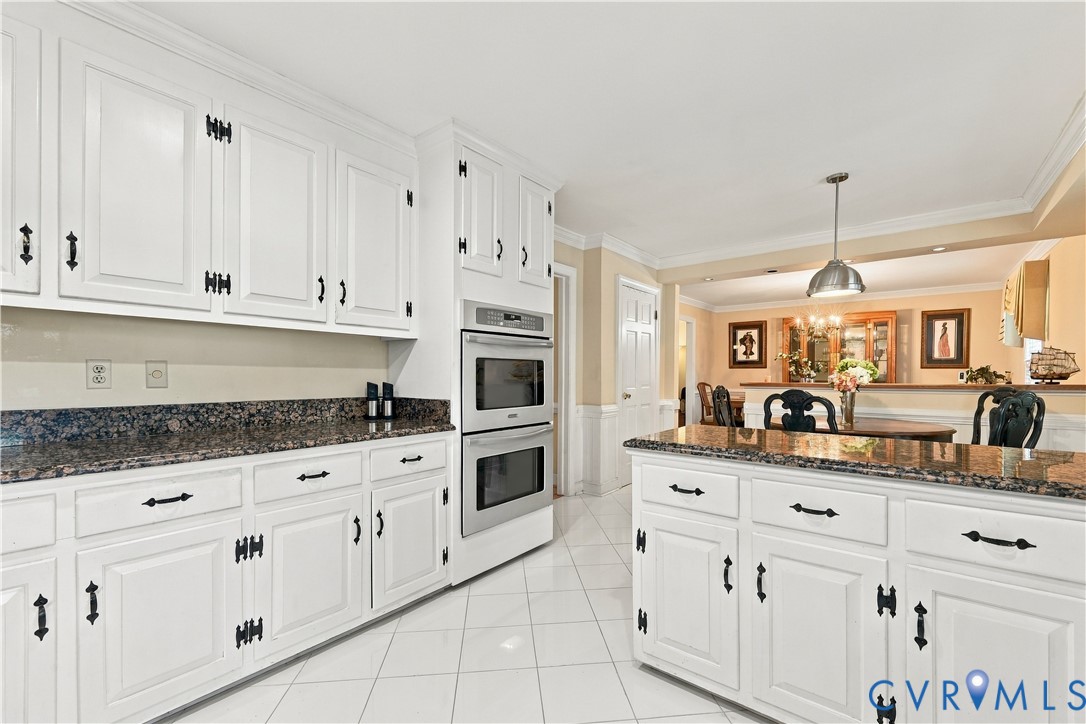 Kitchen featuring white cabinetry, stone countertops, built-in double wall oven, central island, and tile flooring