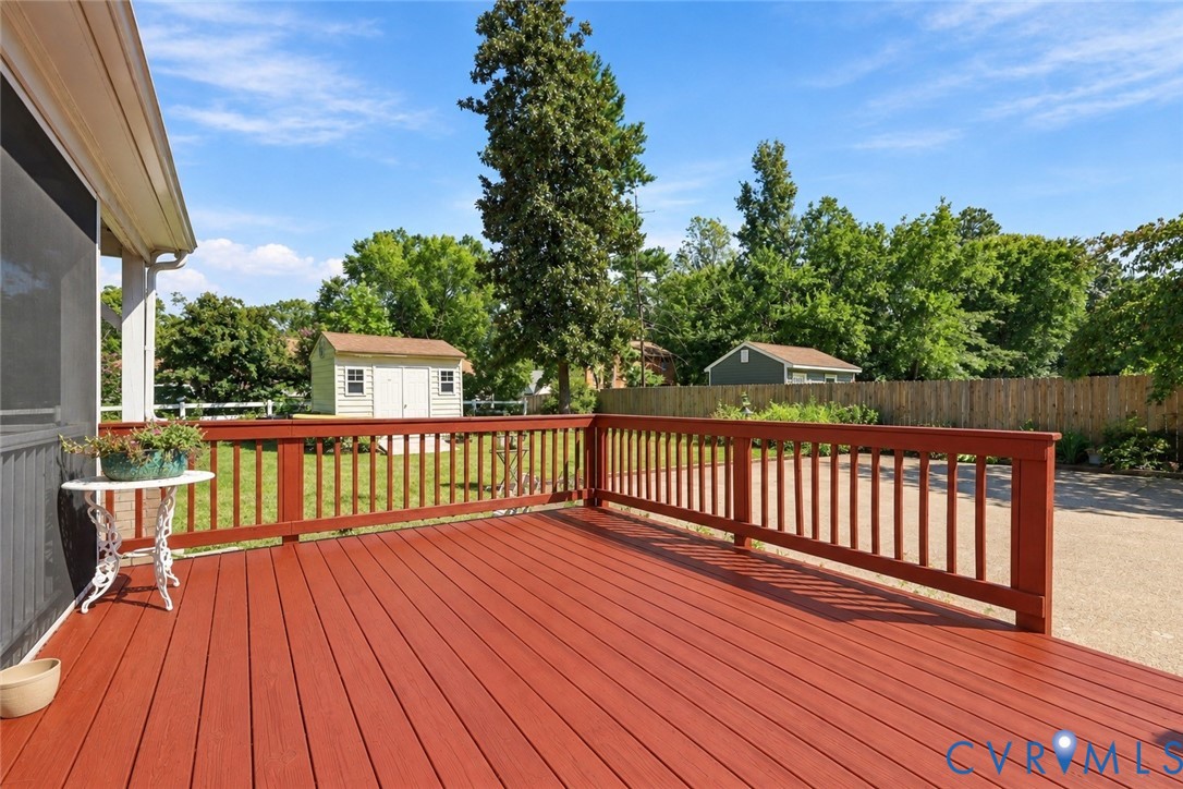 Elevated wood-finish deck with railings, spacious backyard, wooden privacy fencing, and detached storage shed
