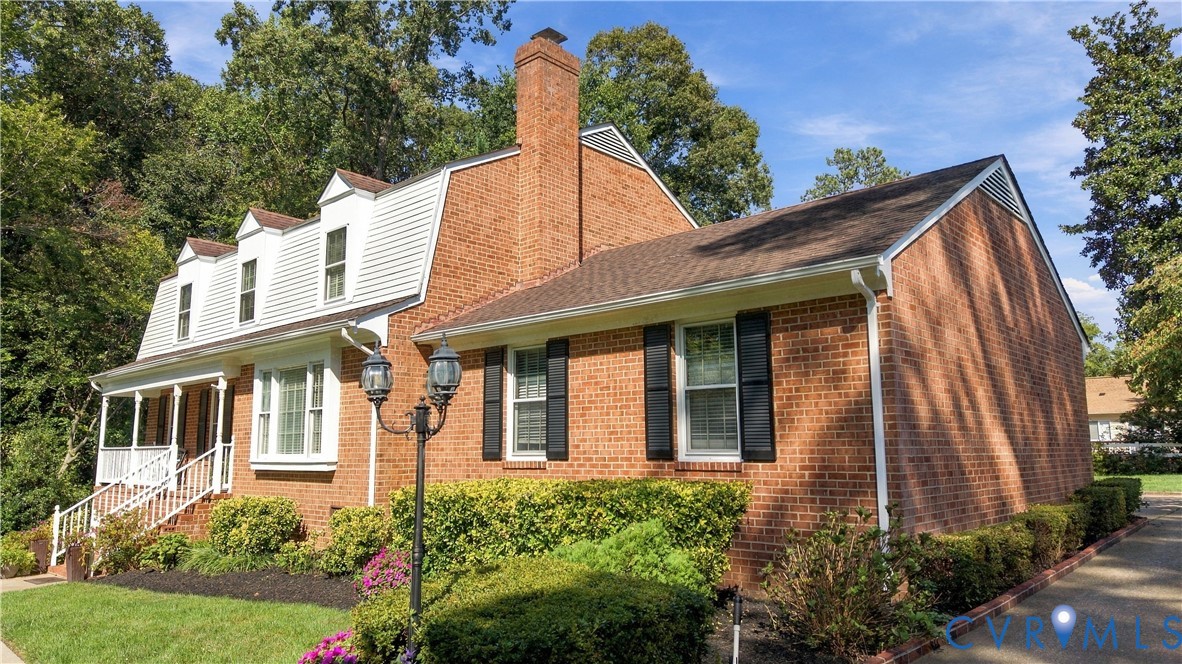 Traditional brick exterior featuring a gambrel roof, dormer windows, a tall chimney, and a covered front porch with white railing