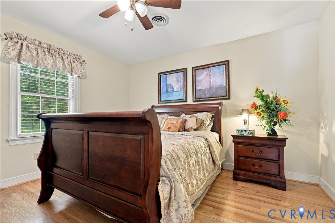 Room featuring wood-finish flooring, a multi-pane window with wood trim, and a ceiling fan with integrated lighting
