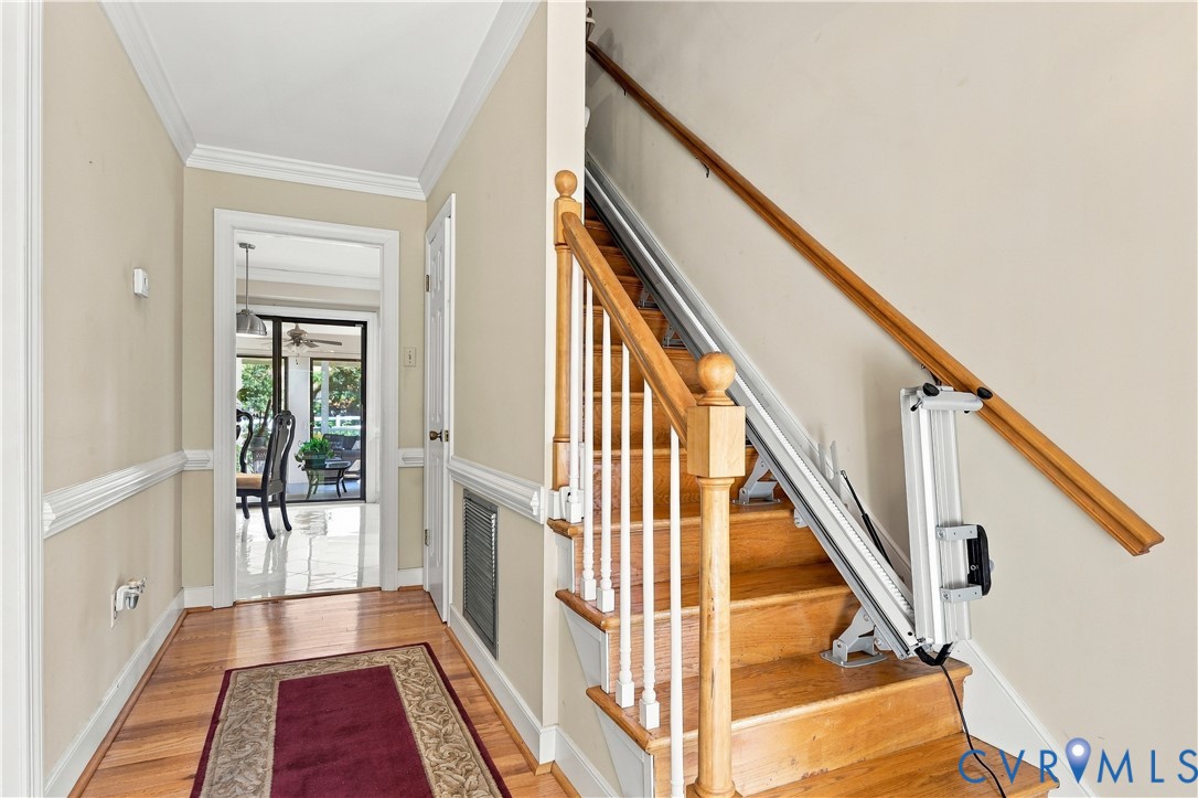 Foyer featuring wood-finish flooring, staircase with a wood handrail, chair rail molding, and a mounted stair lift