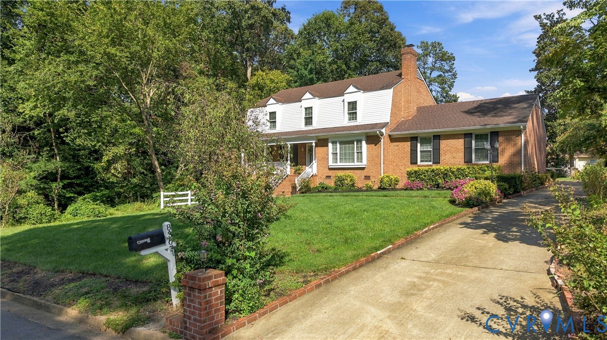 Traditional brick and siding exterior featuring a multi-gabled roofline, concrete driveway, and covered front entryway with architectural columns